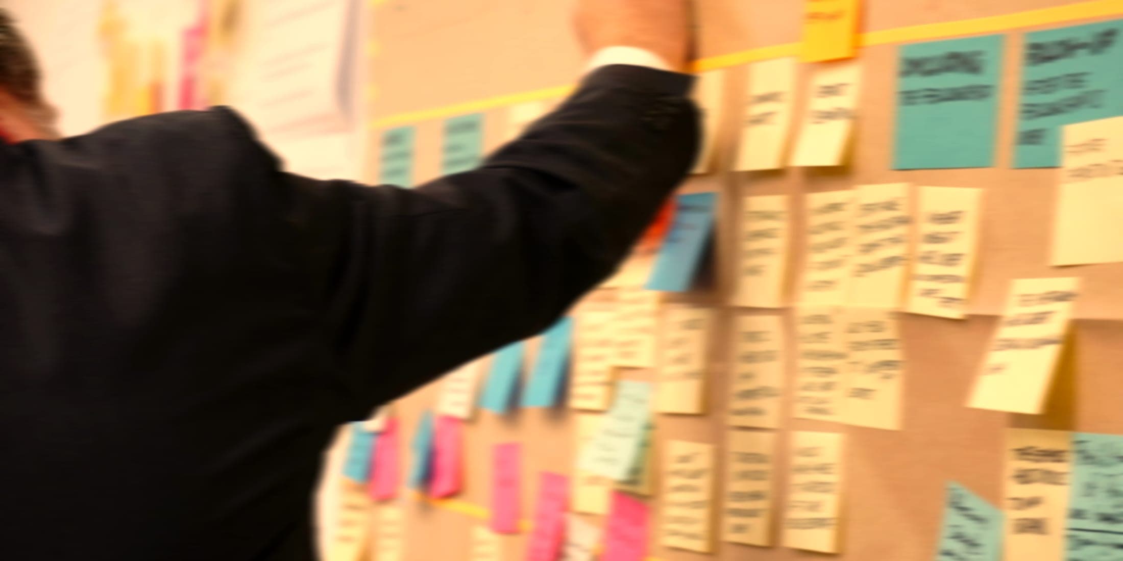 A person arranging handwritten sticky notes on a project wall.