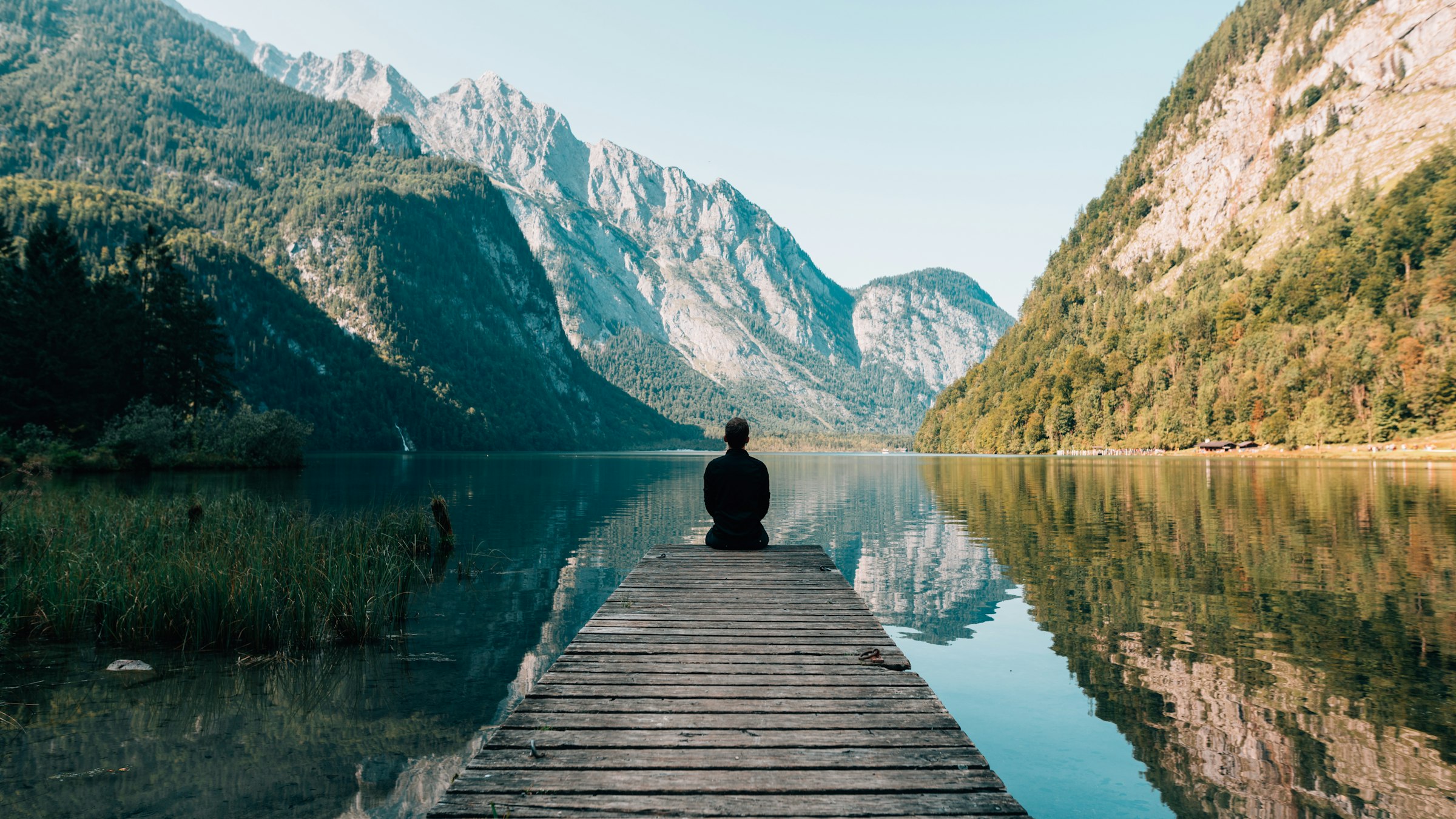 A man sitting at the end of a wooden pier on a mountain lake.